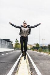 Punk woman screaming and jumping on a barrier at the roadside - GIOF04427