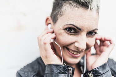 Portrait of smiling punk woman listening to music with earbuds - GIOF04439