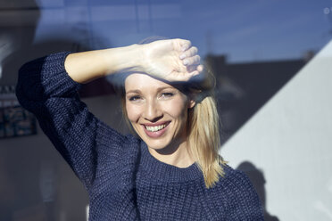 Porträt einer glücklichen blonden Frau, die aus dem Fenster schaut - PNEF00940