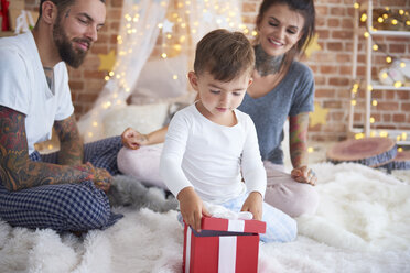 Boy opening Christmas present with his parents in bed - ABIF01040