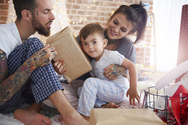 Boy receiving Christmas present from his parents in bed - ABIF01047