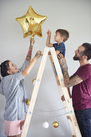 Moderne Familie schmückt das Haus zur Weihnachtszeit mit einer Leiter als Weihnachtsbaum, lizenzfreies Stockfoto