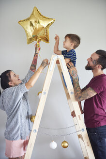 Modern family decorating the home at Christmas time using ladder as Christmas tree - ABIF01059