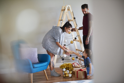 Moderne Familie zu Hause zur Weihnachtszeit mit Leiter als Weihnachtsbaum, lizenzfreies Stockfoto