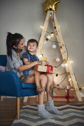 Glücklicher Junge öffnet mit seiner Mutter zu Hause ein Weihnachtsgeschenk - ABIF01070