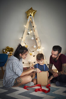Boy opening Christmas present with his parents at home - ABIF01071