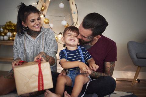 Glücklicher Junge öffnet Weihnachtsgeschenk mit seinen Eltern zu Hause, lizenzfreies Stockfoto