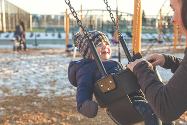 Mother pushing baby son on swing at playground - AURF05480