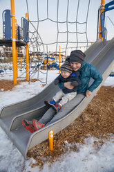 Mutter rutscht mit ihrem kleinen Sohn auf dem Spielplatz die Rutsche hinunter - AURF05482