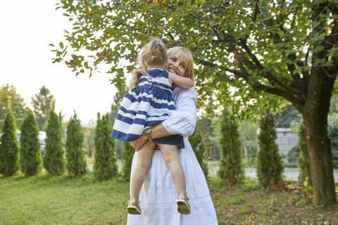 Glückliche Mutter trägt ihre Tochter im Garten, lizenzfreies Stockfoto