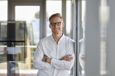 Porträt eines lächelnden Geschäftsmannes im Büro, der sich an ein Fenster lehnt - RBF06709