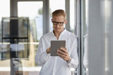 Businessman using tablet at the window in office - RBF06710