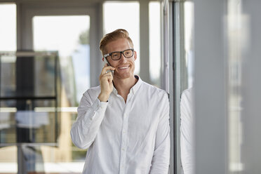 Lächelnder Geschäftsmann am Telefon am Fenster im Büro - RBF06714