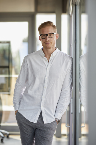 Porträt eines selbstbewussten Geschäftsmannes in einem Büro, der sich an ein Fenster lehnt, lizenzfreies Stockfoto