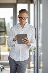 Businessman using tablet at the window in office - RBF06718