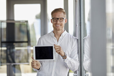 Porträt eines lächelnden Geschäftsmannes, der ein Tablet am Fenster im Büro zeigt - RBF06719