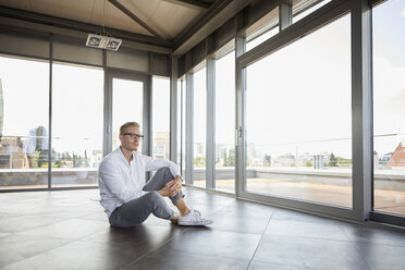 Businessman sitting in empty room looking out of panorama window - RBF06721