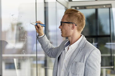 Businessman writing on glass pane in office - RBF06726