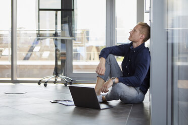 Businessman sitting on the floor next to laptop - RBF06731