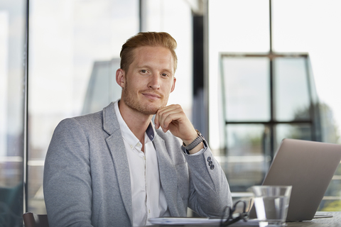 Porträt eines selbstbewussten Geschäftsmannes mit Laptop auf dem Schreibtisch im Büro, lizenzfreies Stockfoto