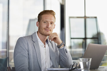 Portrait of confident businessman with laptop on desk in office - RBF06736