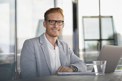 Porträt eines lächelnden Geschäftsmannes mit Laptop auf dem Schreibtisch im Büro - RBF06737