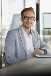 Portrait of smiling businessman sitting at desk in office - RBF06738