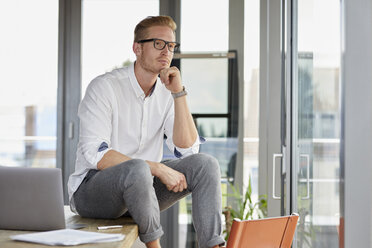 Serious businessman with laptop sitting on desk in office - RBF06746