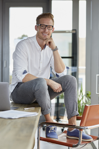 Porträt eines lächelnden Geschäftsmannes mit Laptop auf dem Schreibtisch im Büro, lizenzfreies Stockfoto