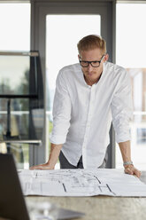 Young man working on blueprint on desk in office - RBF06749