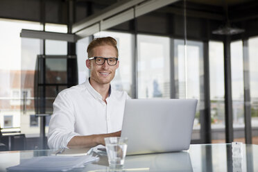 Portrait of smiling businessman using laptop on desk in office - RBF06753