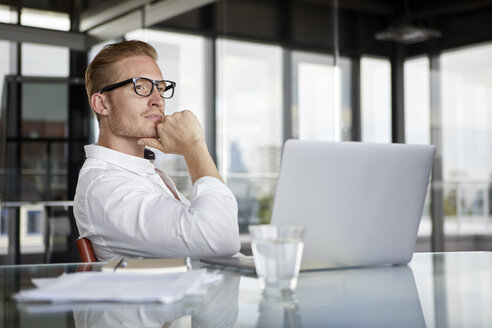 Businessman with laptop on desk in office thinking - RBF06755