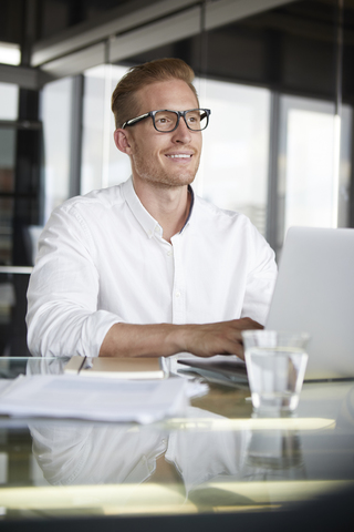 Lächelnder Geschäftsmann mit Laptop auf dem Schreibtisch im Büro, lizenzfreies Stockfoto