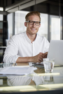 Porträt eines lächelnden Geschäftsmannes mit Laptop auf dem Schreibtisch im Büro - RBF06758