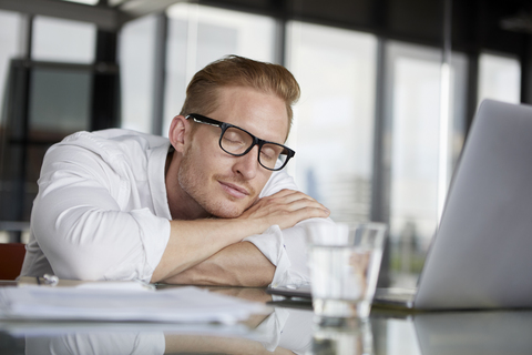 Businessman leaning on desk in office with closed eyes stock photo