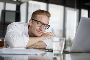 Businessman leaning on desk in office with closed eyes - RBF06761