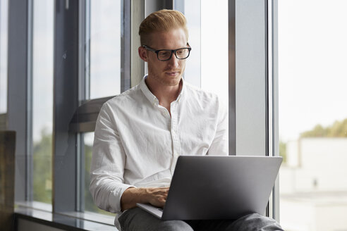 Geschäftsmann sitzt auf der Fensterbank und benutzt einen Laptop - RBF06768