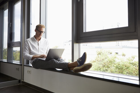 Geschäftsmann sitzt auf der Fensterbank und benutzt einen Laptop - RBF06769