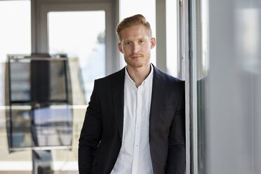 Portrait of confident businessman in office leaning against window - RBF06776