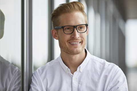 Porträt eines lächelnden Geschäftsmannes, der am Fenster lehnt, lizenzfreies Stockfoto