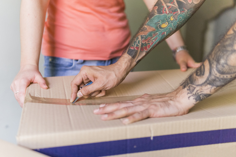 Männerhand öffnet Kartonschachtel mit Taschenmesser im neuen Zuhause, Teilansicht, lizenzfreies Stockfoto