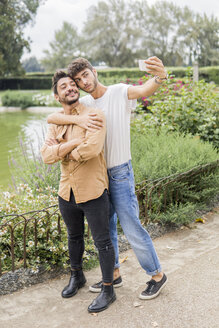 Porträt eines jungen schwulen Paares, das im Stadtpark ein Selfie mit seinem Smartphone macht - FBAF00057