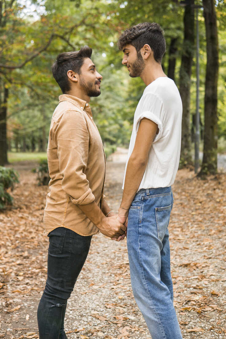 Happy young gay couple holding hands in autumnal park stock photo