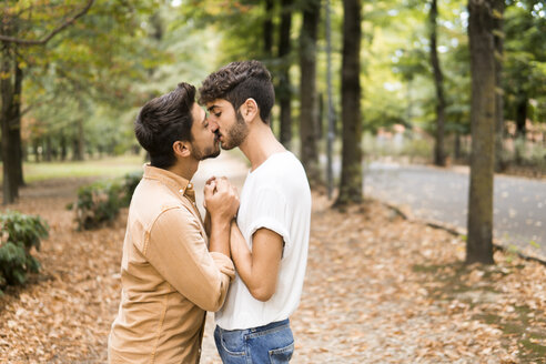 Junges schwules Paar hält Hände und küsst sich im herbstlichen Park - FBAF00068