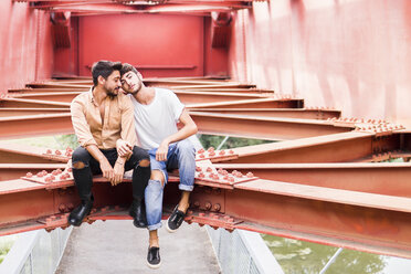 Junges verliebtes schwules Paar sitzt auf dem Stahlträger einer Fußgängerbrücke - FBAF00074