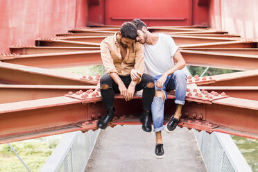 Young gay couple in love sitting on steel girders of a footbridge - FBAF00075