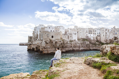 Italien, Apulien, Polognano a Mare, Rückenansicht eines Mannes, der sich auf einem Felsen ausruht und auf den Horizont schaut - FLMF00035