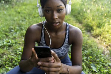 Junger Sportler in der Natur, hört Musik mit Kopfhörern, hält Smartphone - GIOF04449