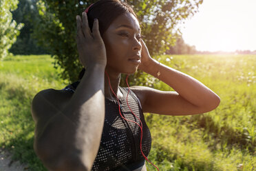 Junger Sportler in der Natur, der mit Kopfhörern Musik hört und sich auf das Training vorbereitet - GIOF04467