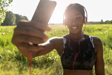 Junger Sportler in der Natur, hört Musik mit Kopfhörern, hält Smartphone - GIOF04469